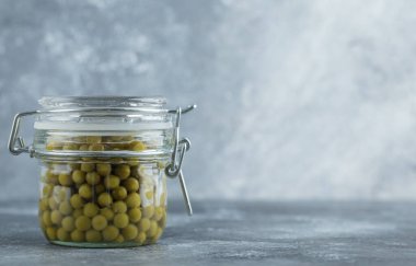 Gri arkaplanda kavanozdaki turşulu zeytinlerin yakın plan fotoğrafı.