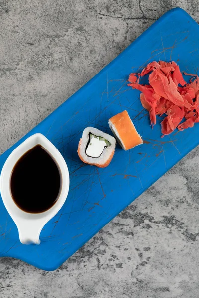 Deliciosos rollos de sushi de Filadelfia, salsa de soja y jengibre en la tabla de cortar azul — Foto de Stock