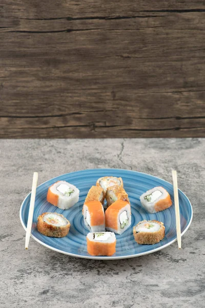Placa azul de deliciosos rollos de sushi sobre fondo de mármol — Foto de Stock