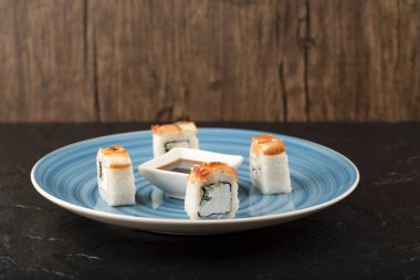 Lezzetli ejderha suşi ruloları ve mavi tabakta soya sosu.