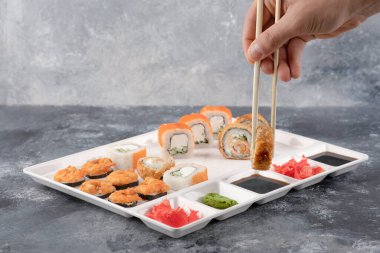 Beyaz tabaktaki çubuklarla suşi yiyen bir erkek.