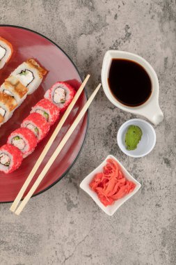 Kırmızı tabak dolusu suşi, wasabi ve mermer masa üzerinde turşu.