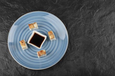 Lezzetli ejderha suşi ruloları ve mavi tabakta soya sosu.