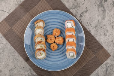 Mermer masada çeşitli suşi rulolarından oluşan mavi tabak.