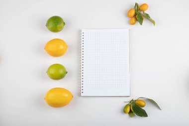 Beyaz kağıt etrafında taze limon, kumkat ve limon.