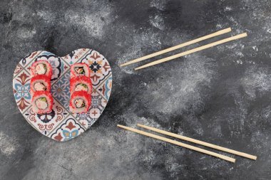 Kalp şeklinde tabakta kırmızı havyarla lezzetli suşi ruloları.