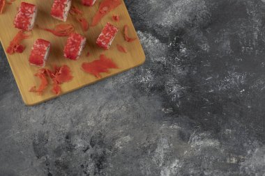 Kaliforniya suşi ruloları ve ahşap tahtaya saçılmış zencefil turşusu.