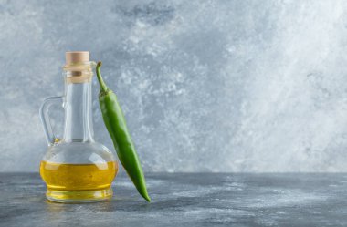 Yeşil biber ve gri arka planda bir şişe yağ.