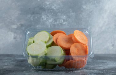 Dilimlenmiş kabak ve havuç gri arka planda plastik kabın içinde.