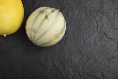 Siyah yüzeyde taze sarı ve yeşil kavunlar.