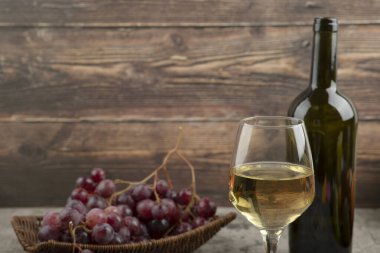 Kırmızı üzüm sepeti ve mermer masada beyaz şarap.