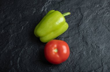 Siyah zemin üzerinde taze organik domates ve biber resmi.
