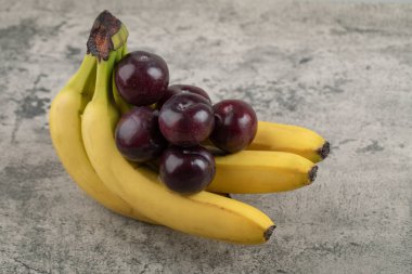 Taş zemin üzerinde muz kümesi olan taze, sağlıklı erikler.