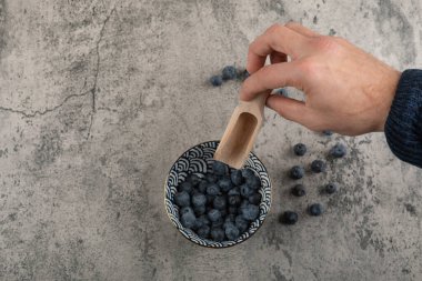 Yaban mersini kasesinin üstünde kaşığı tutan bir erkek.