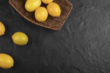 Siyah yüzeyde bir sepet dolusu taze limon.