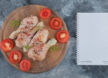 Ahşap tahtaya çiğ tavuk budu ve taze domates koyun.