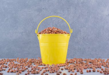 Kırmızı fasulye dolu sarı kova mermer arka planda dağınık bir yığın arasında. Yüksek kalite fotoğraf