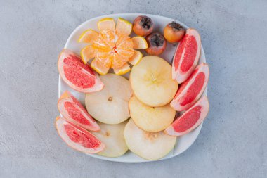 Bir tabak dilimlenmiş greyfurt, armut ve mermer zemin üzerinde soyulmuş mandalina. Yüksek kalite fotoğraf