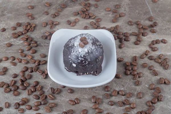 Scattered coffee beans around a small platter with a chocolate coated cake on marble background. High quality photo