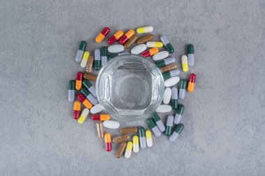 Bir bardak saf su ve gri arka planda renkli haplar. Yüksek kalite fotoğraf