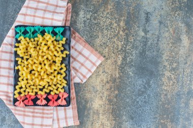 Farfalle ve kıvırcık makarna tabakta, havlunun üstünde, mermer zemin üzerinde. Yüksek kalite fotoğraf