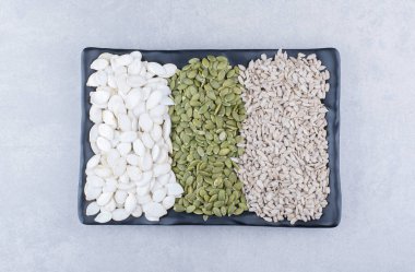 Assorted plate of pepitas, sunflower seeds and white pumpkin seeds on marble background. High quality photo