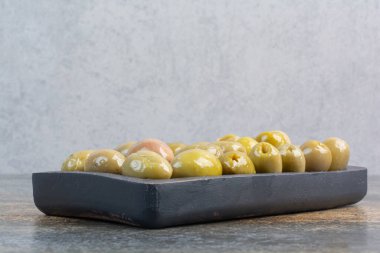 Mermer zemin üzerinde tuzlu ve lezzetli zeytinlerden oluşan karanlık bir tahta. Yüksek kalite fotoğraf