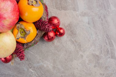 Kırmızı kozalaklı taze meyve sepeti ve mermer arka planda noel ağacı süslemeleri. Yüksek kaliteli illüstrasyon