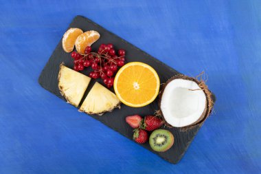 Mavi arka planda dilimlenmiş lezzetli meyvelerden oluşan siyah bir tahta. Yüksek kalite fotoğraf