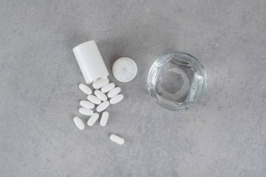 Gri arka planda bir bardak saf su bulunan beyaz haplardan oluşan küçük bir kavanoz. Yüksek kalite fotoğraf