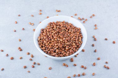 Beyaz kâse kırmızı fasulye mermer arka planda dağınık bir fasulye yığınının ortasında duruyor. Yüksek kalite fotoğraf