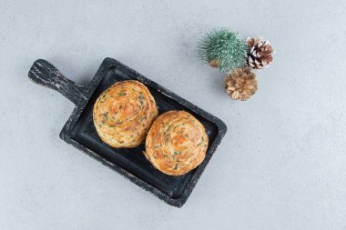 Çam kozalaklarının yanında siyah bir tepside ekşi goglar ve mermer arka planda bir ağaç heykelciği. Yüksek kalite fotoğraf