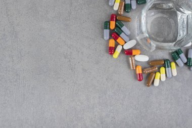 Bir bardak saf su ve gri arka planda renkli haplar. Yüksek kalite fotoğraf