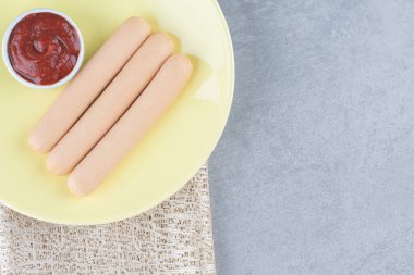 Taze haşlanmış sosis ve gri arka planda sarı tabakta ketçap. Yüksek kalite fotoğraf