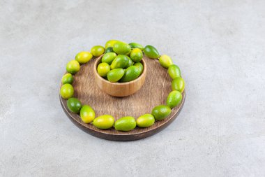 Tahta bir tahtanın üzerinde mermer arka planda kumkatlarla çevrili bir kase kumkat. Yüksek kalite fotoğraf