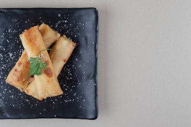 Mermer arka planda siyah bir tabağa sarılmış gözleme paketleri. Yüksek kalite fotoğraf