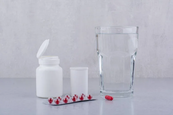 Red pills, containers and glass of water on marble surface. High quality photo