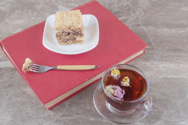 A small serving of cake on a book next to a cup of tea on marble background. High quality photo