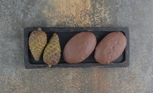 Chocolate coated cakes and pine cones in a small tray on wooden background. High quality photo