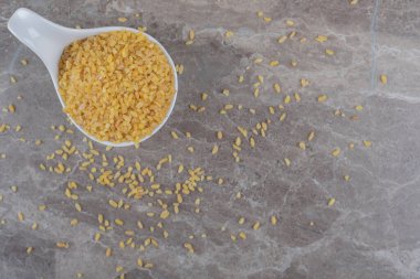 Mermer arka planda bir kaşık dolusu bulgurs ve dağınık bulgurlar. Yüksek kalite fotoğraf