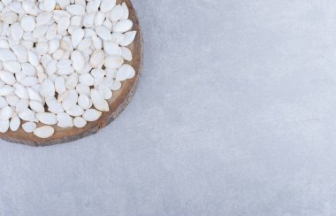 Dilimlenmiş odun parçasında mermer zemin üzerinde küçük beyaz balkabağı tohumları yığını. Yüksek kalite fotoğraf