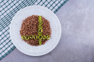 Mermer zemin üzerinde süslü bir tabakta biber dilimli pişmiş karabuğday porsiyonu. Yüksek kalite fotoğraf