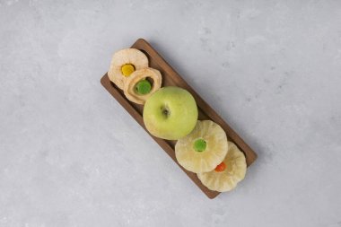 Tahtada taze yeşil elma ve kurutulmuş ananas dilimleri, kurabiyeler ve jöleler.