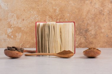 İçinde kahve çekirdeği ve kakao tozu dolu tahta kaşıklar olan açık bir kitap. Yüksek kalite fotoğraf