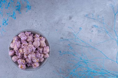 Mor patlamış mısır şekeriyle dolu küçük kase mermer arka planda dekoratif dalların yanında. Yüksek kalite fotoğraf