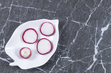 Siyah zemin üzerinde seramik tabakta üç taze turp dilimi. Yüksek kalite fotoğraf