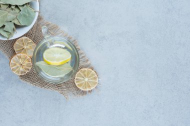 Limonata ve dilimlenmiş limon havlunun üzerindeki bir kase yaprağın yanında, mermer zemin üzerinde. Yüksek kalite fotoğraf