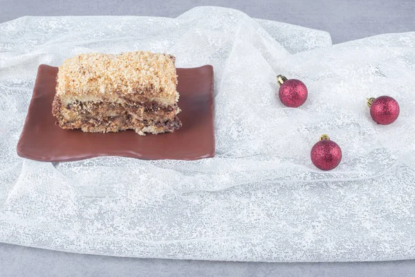 Slice of cake on a platter next to baubles on tablecloth on marble background. High quality photo