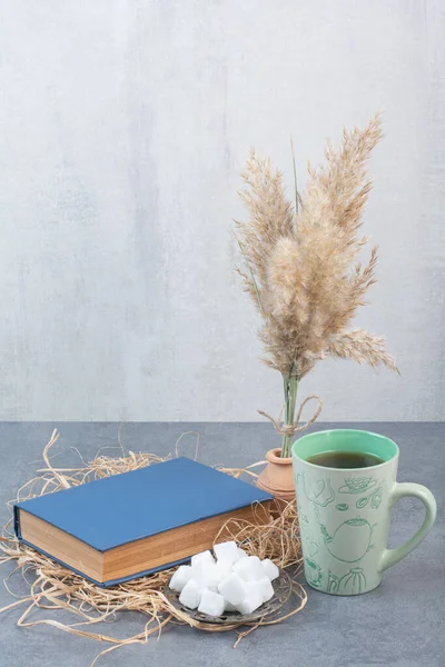 A cup of delicious tea with book and sugar on hay. High quality photo