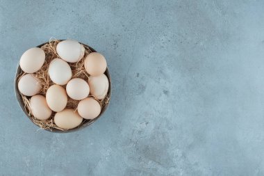Mermer arka planda bir kasede saman yığını üzerinde bir tomar yumurta. Yüksek kalite fotoğraf